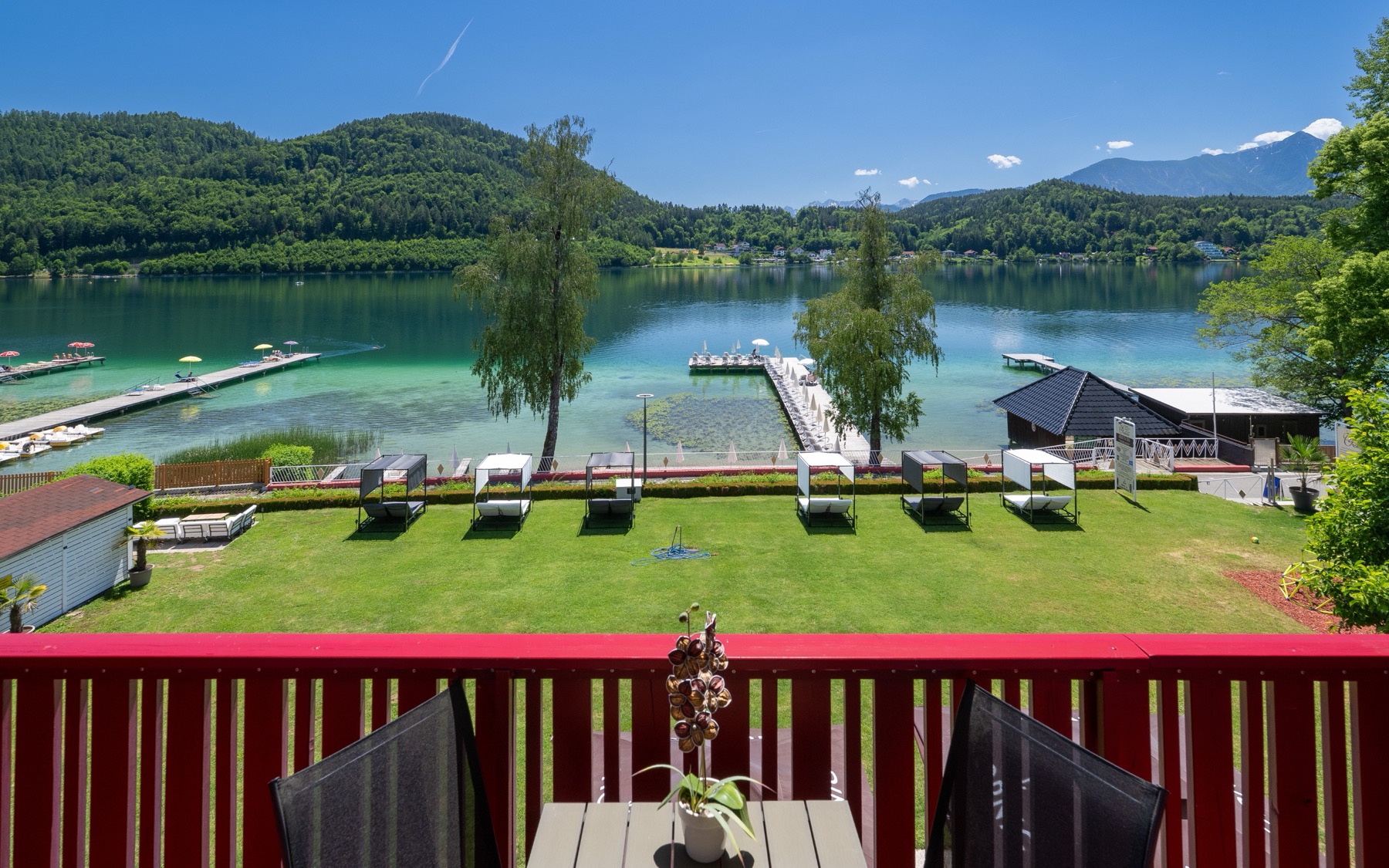 Blick vom Hotelbalkon über die Liegewiese mit Himmelbetten auf den türkisen Klopeiner See